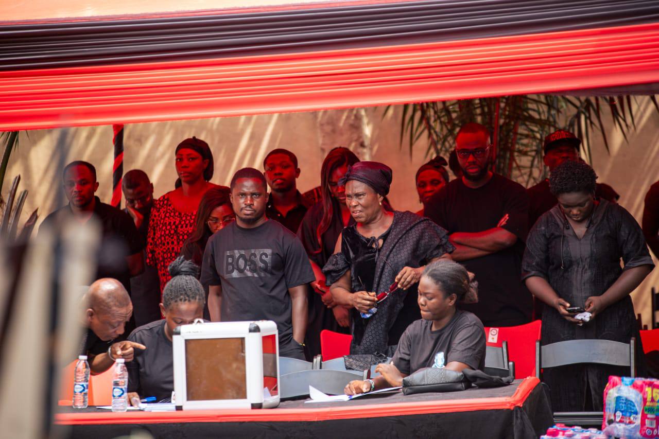 Family members gathered in unity behind the central coordination table framed by traditional red and black canopy drapery.